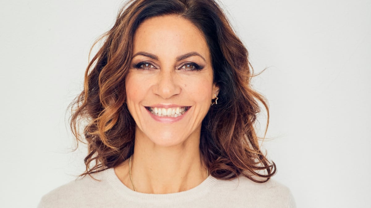 This is a headshot photograph of walking and wellness warrior Julia Bradbury. She has gorgeous flowing brunette hair, and her smile beams off the screen. This photograph is part of the UK's Walk Yourself Happy Retreats campaign.